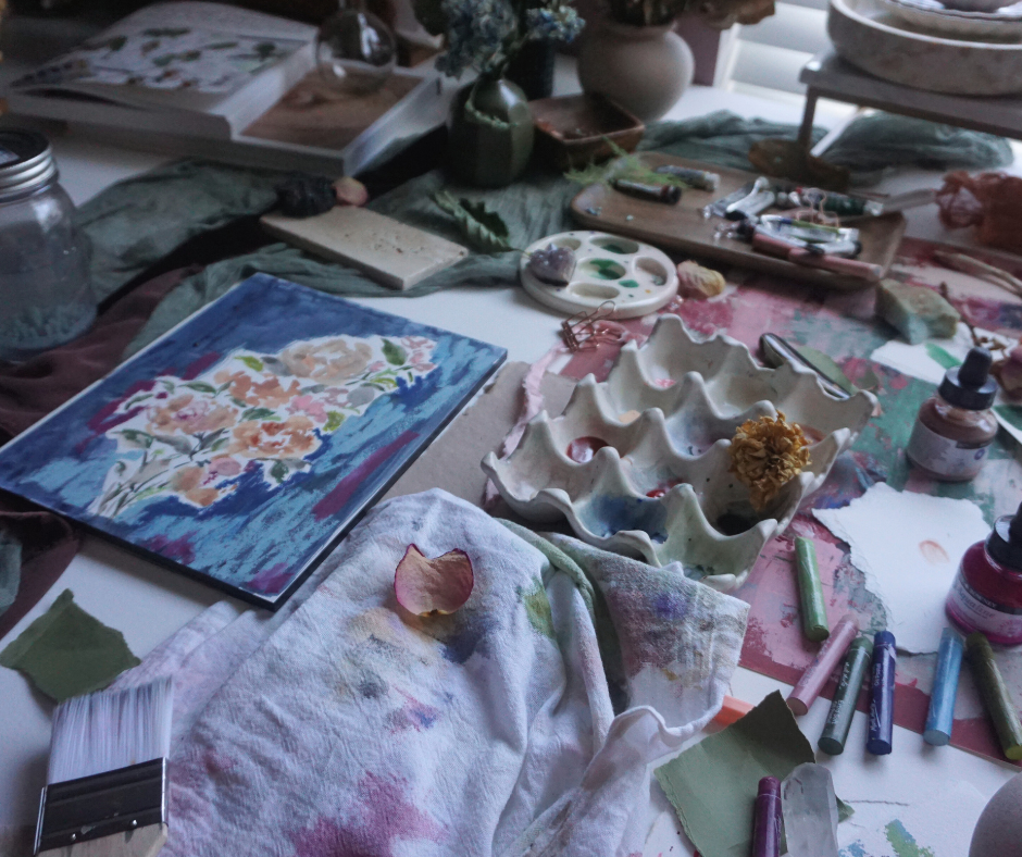 Artist table with watercolor florals on a blue background. The art table also has various art supplies including watercolor brushes, a paint palette and oil pastels