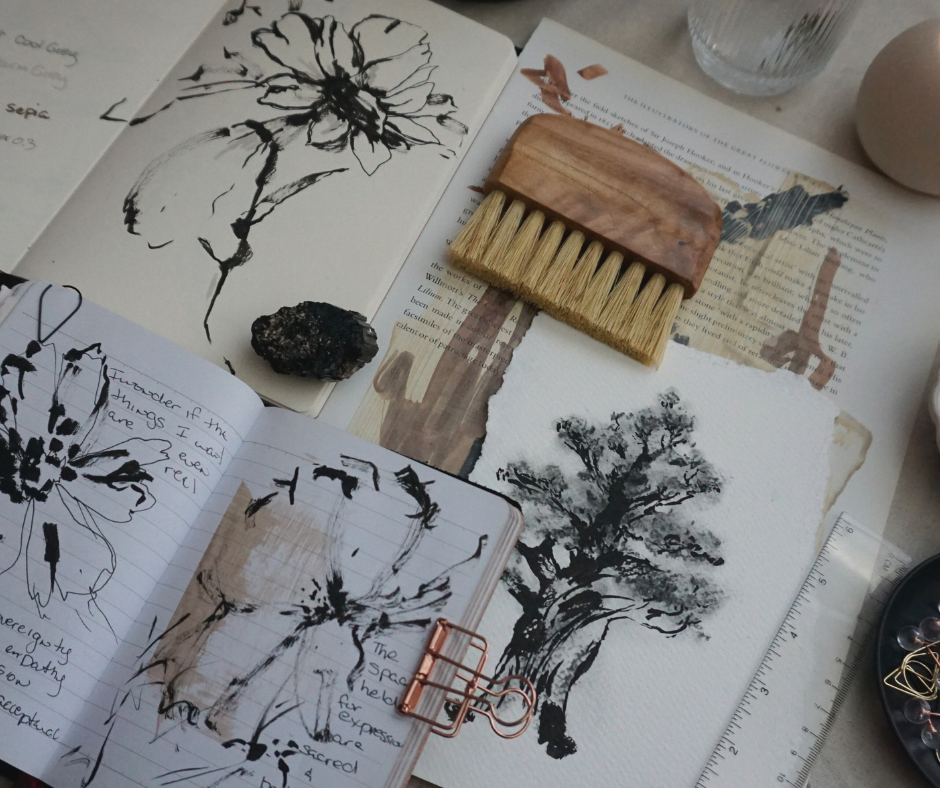 artist table with art journal containing black and white floral and tree sketches