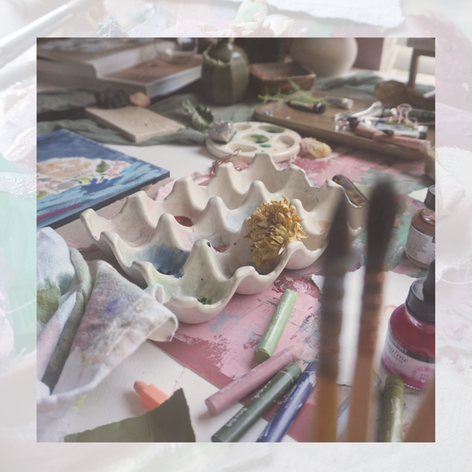 artist table with art palette, paintbrushes, oil pastels and a blue floral painting
